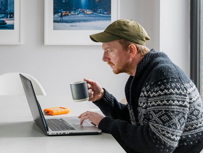 男人坐在厨房的桌子上喝着咖啡，在家上在线课程