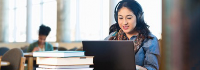 一位女士在图书馆戴着耳机用笔记本电脑学习